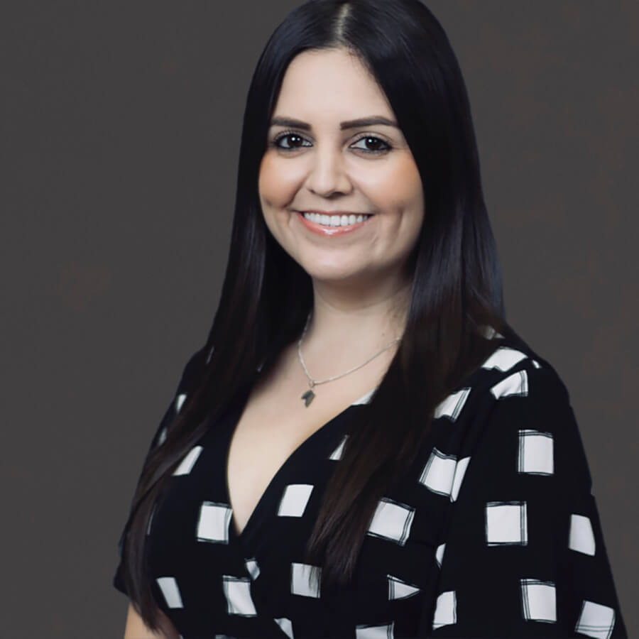 Smiling woman in black and white patterned dress against a dark background.