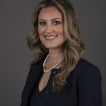 Professional woman smiling in a dark blazer and pearl necklace.