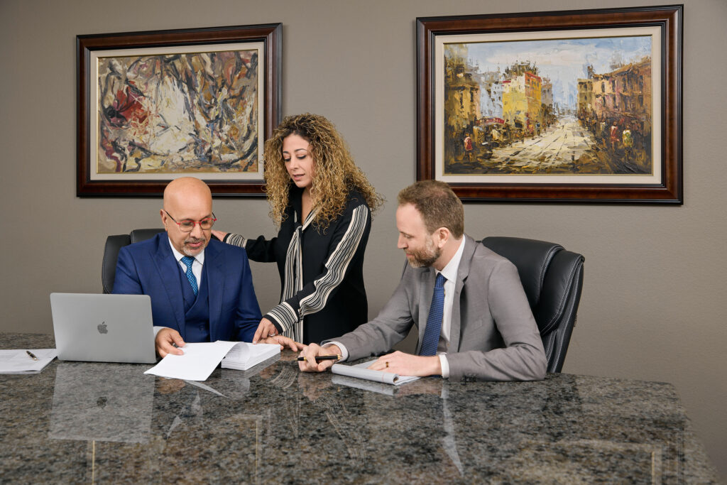 Three Madison Law partner's collaborate at a marble conference table, reviewing legal documents in a professional office setting.