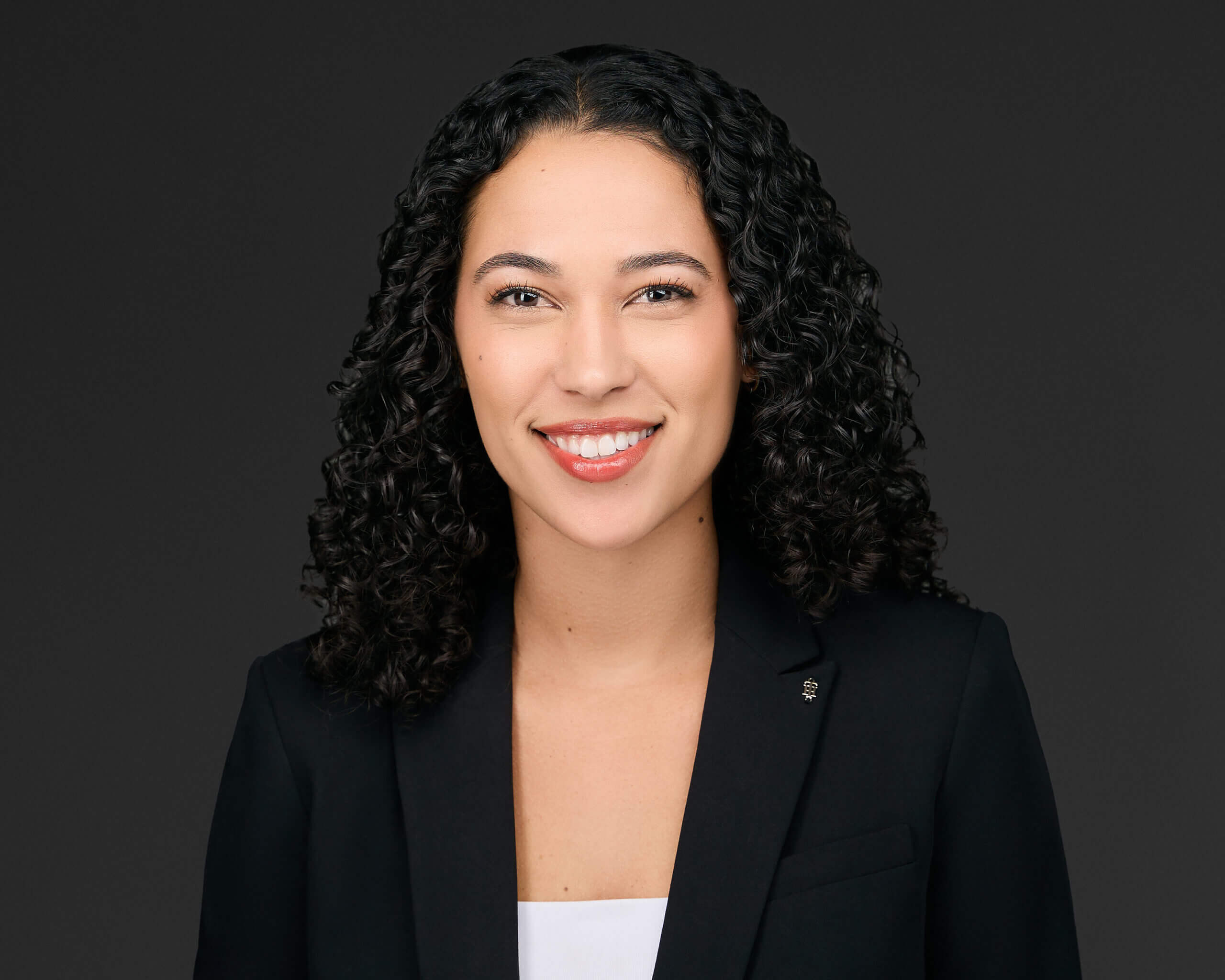Professional headshot of a woman with curly hair wearing a black blazer.