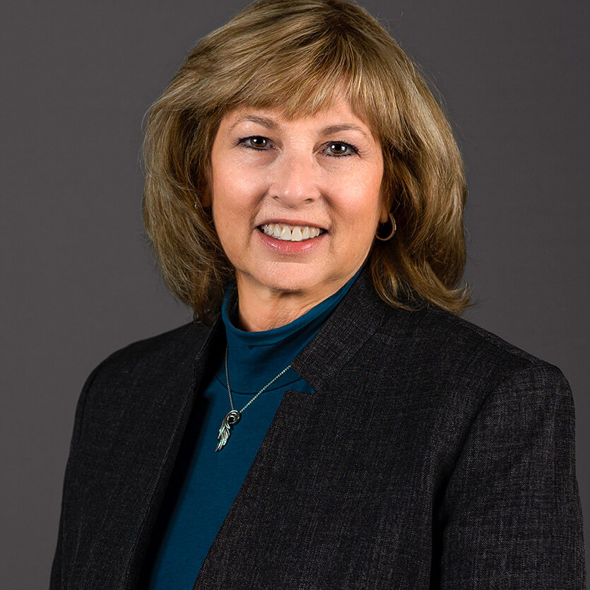 Professional portrait of a smiling woman in business attire against a gray background.