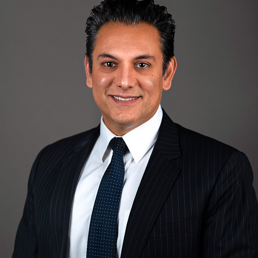 Professional man in a dark suit and tie smiling at the camera.