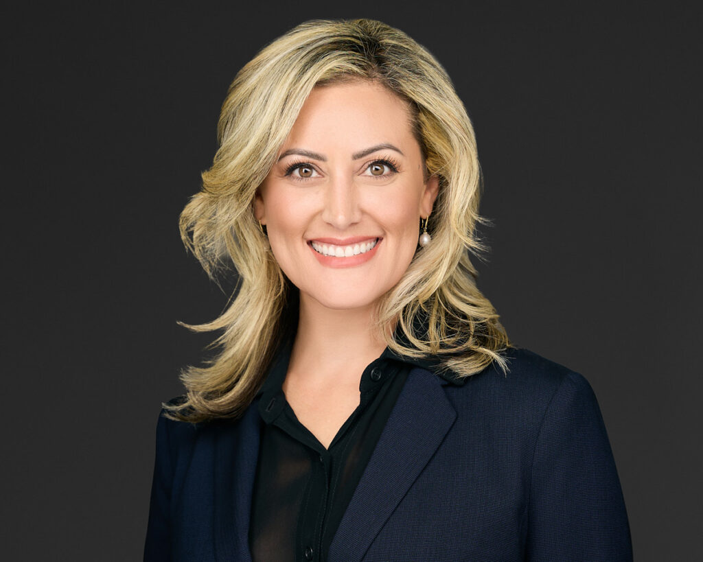 Professional woman smiling confidently in business attire against a dark background.