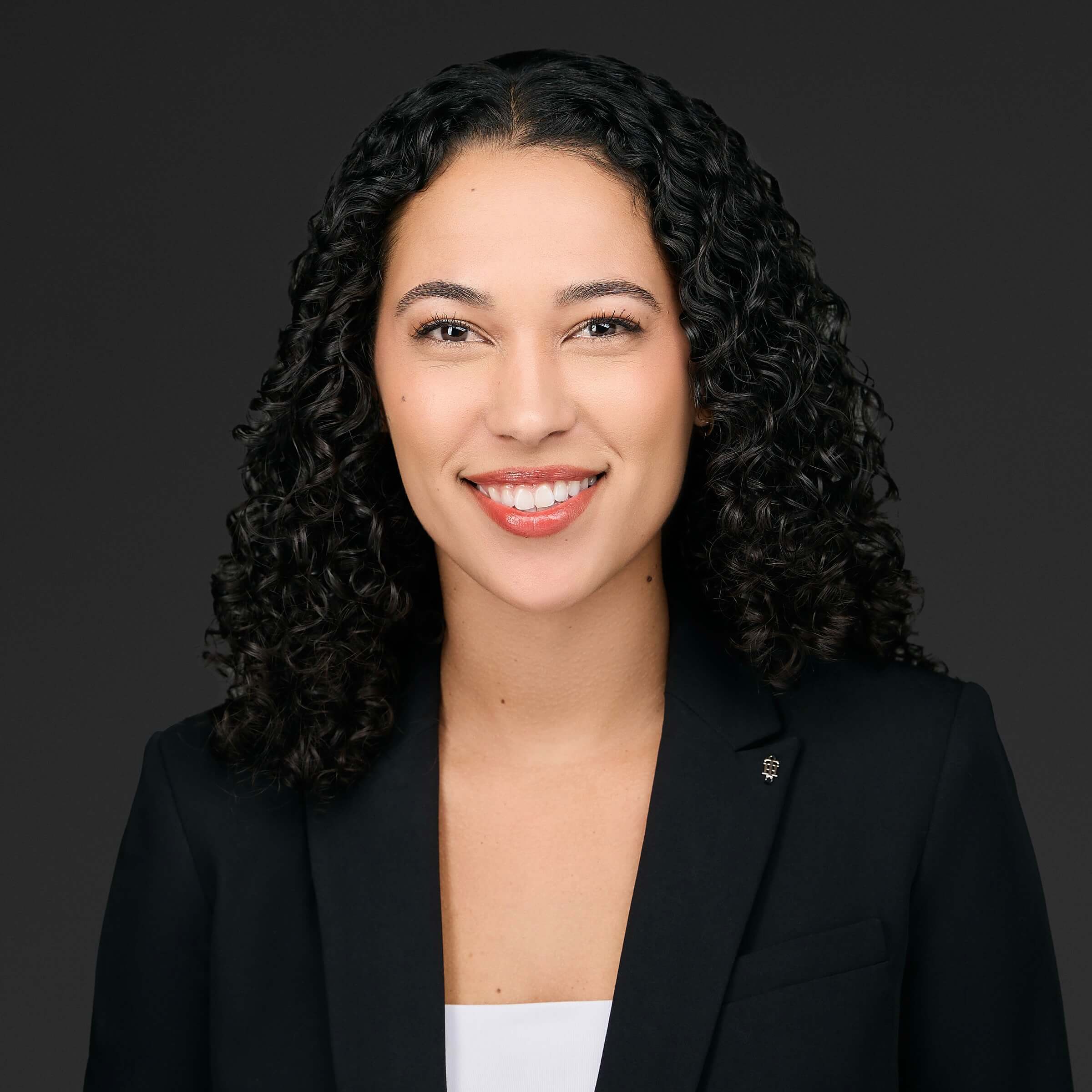Professional woman with curly hair smiling against a dark background.