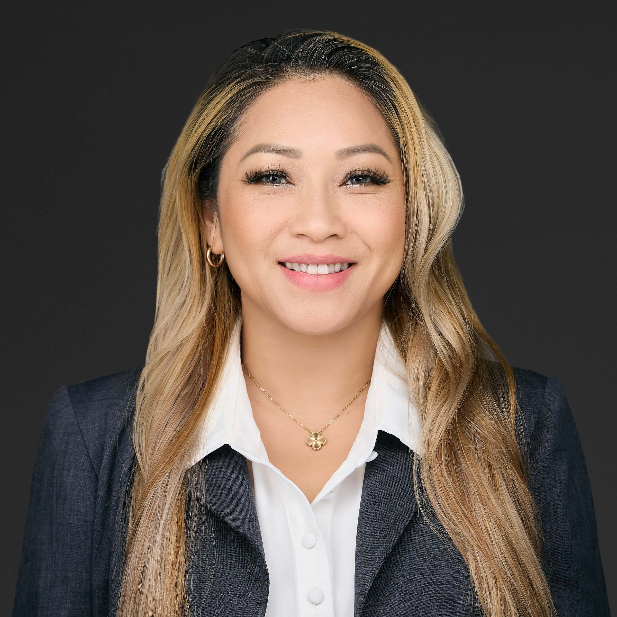 Professional woman with long blonde hair in business attire smiles against a dark background.