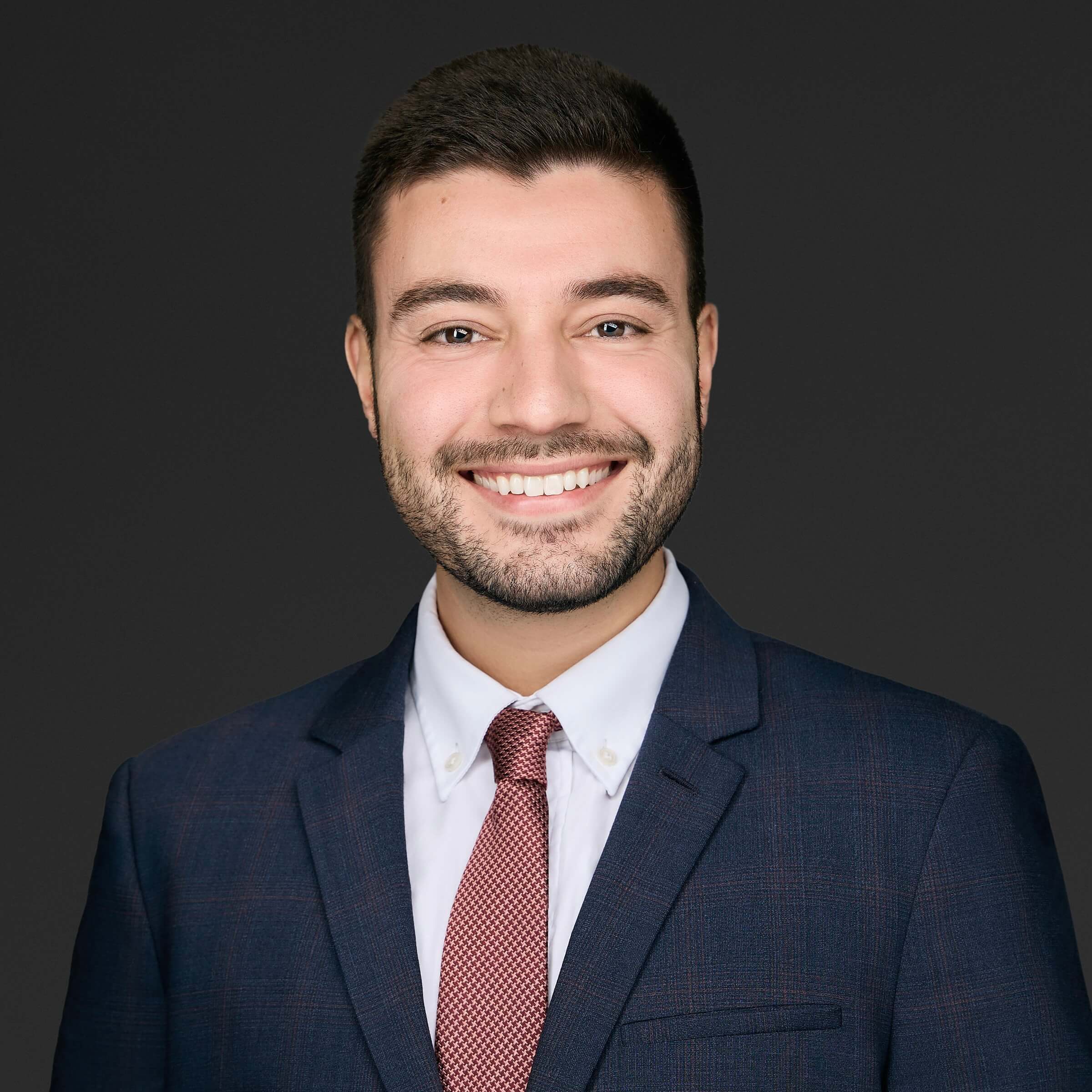 Professional man in a suit smiling against a dark background.
