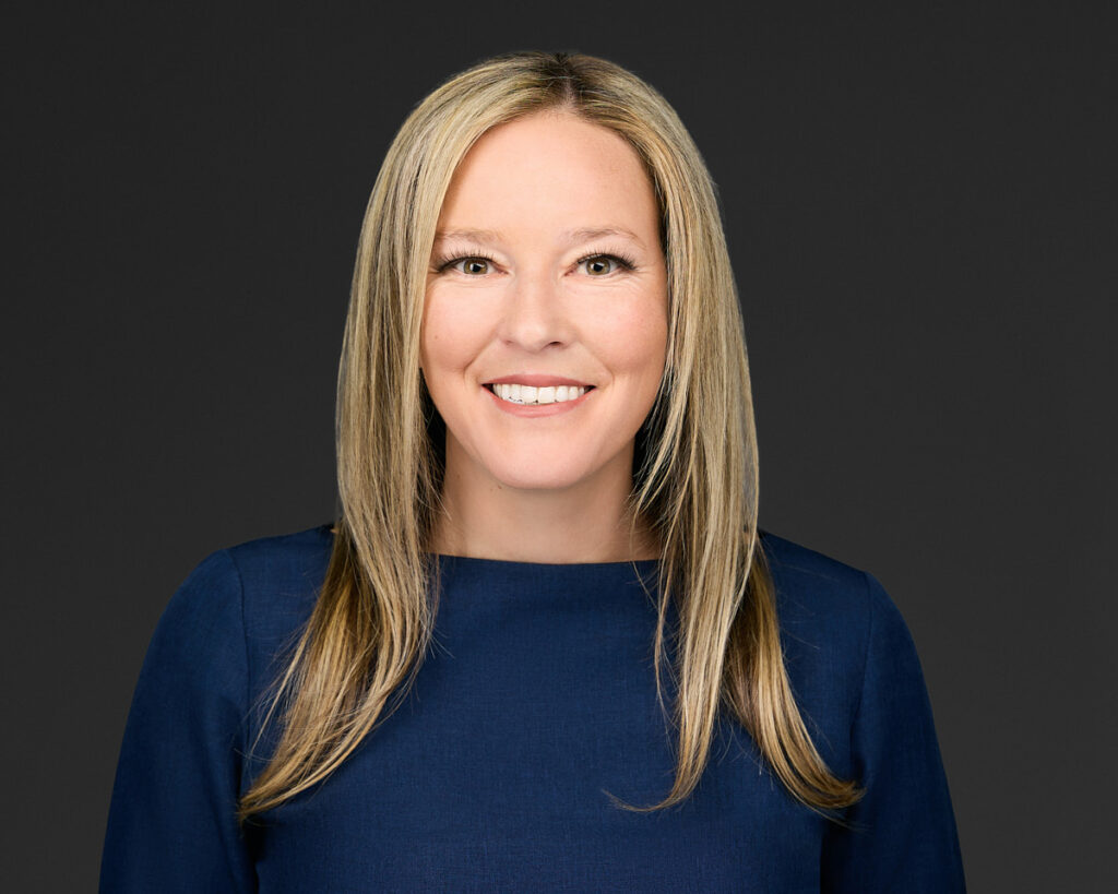 Professional portrait of a smiling woman with blonde hair and a navy blue top.