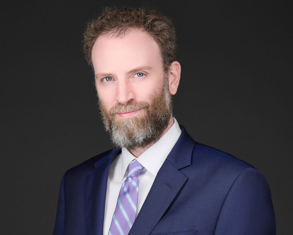 Professional headshot of Brett K. Wiseman, Esq., Partner at Madison Law, wearing a navy suit and lavender-striped tie, with a confident expression.