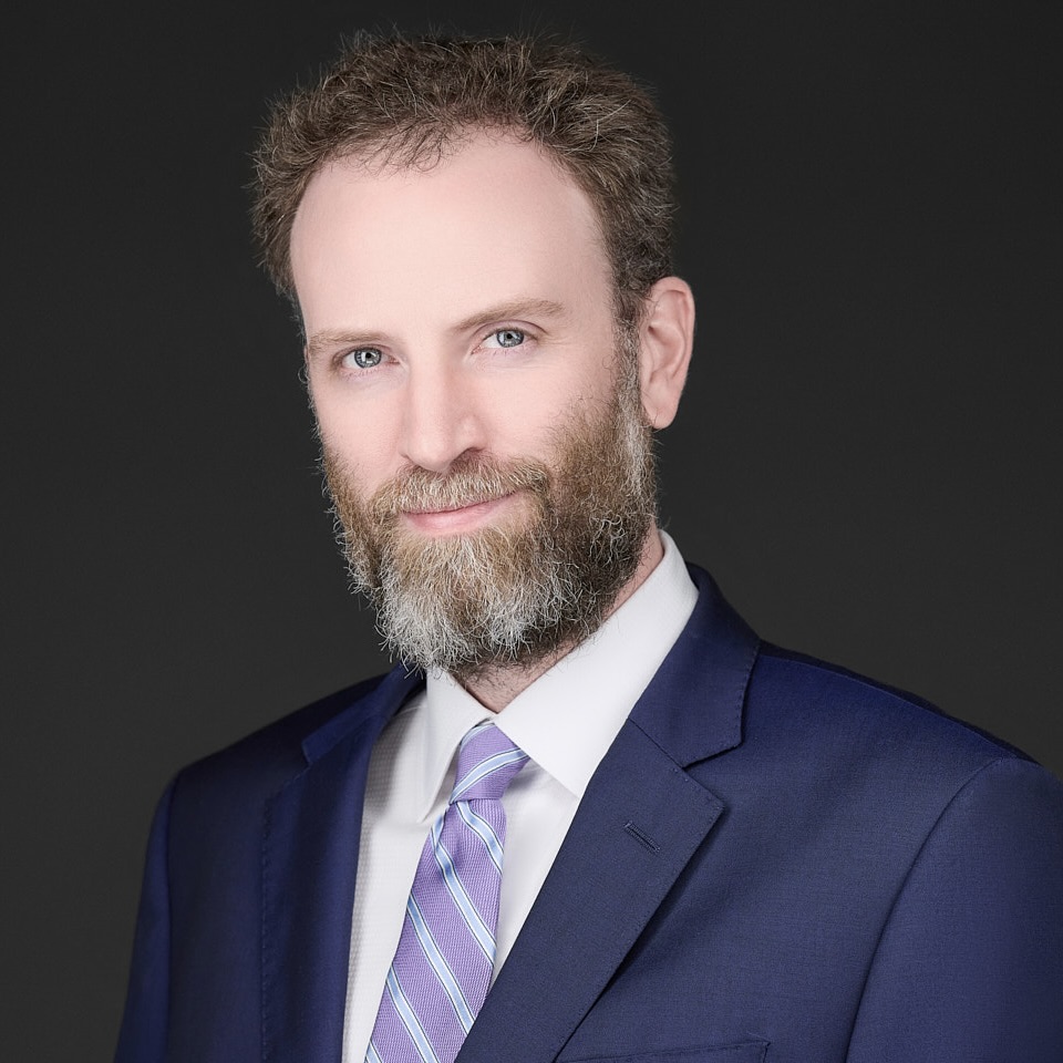 Professional headshot of Brett K. Wiseman, Esq., Partner at Madison Law, wearing a navy suit and lavender-striped tie, with a confident expression.