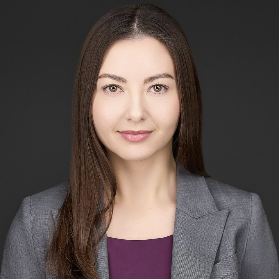 Professional woman with long brown hair in a business suit against a dark background.