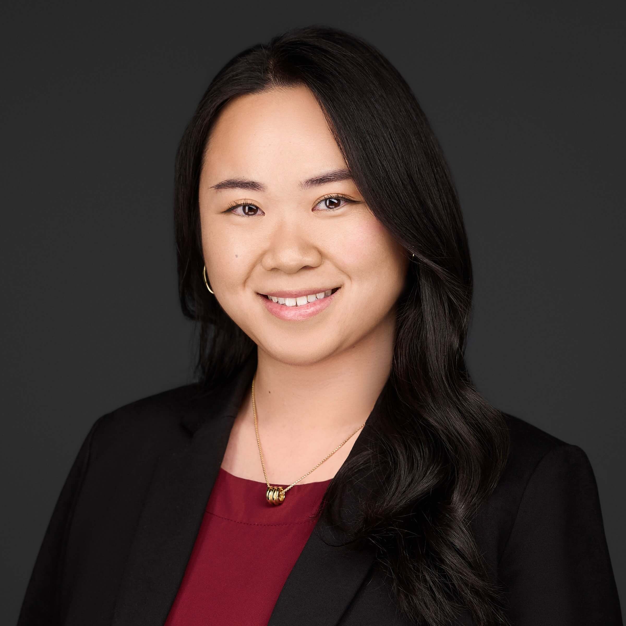 Professional headshot of a smiling young woman with dark hair wearing business attire.