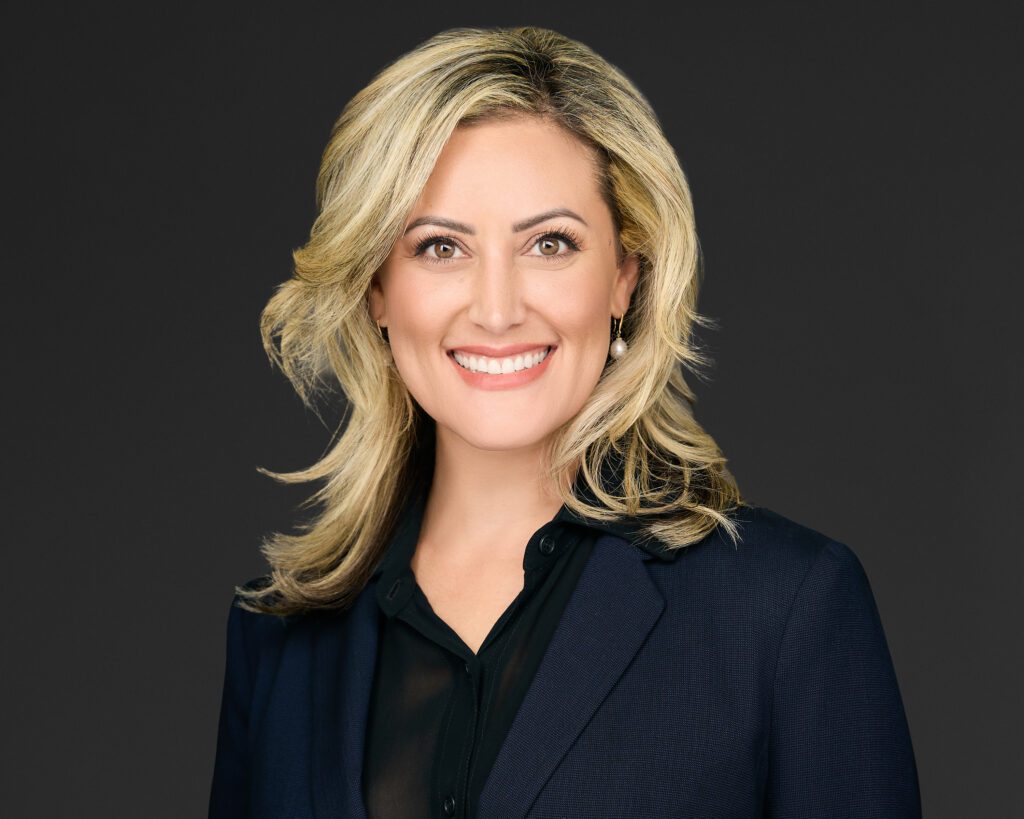 Professional woman smiling in business attire against a dark background.