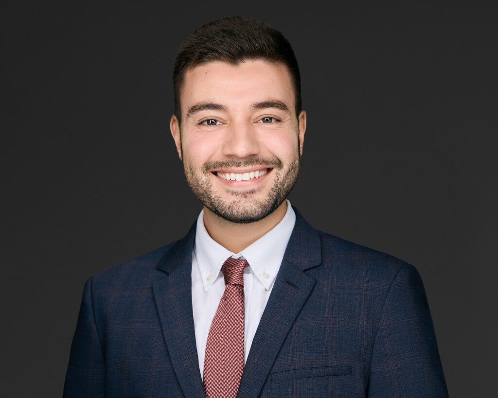 Smiling young man in a suit and tie against a dark background.